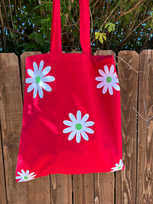 red tote bag with white flowers in front of brown fence