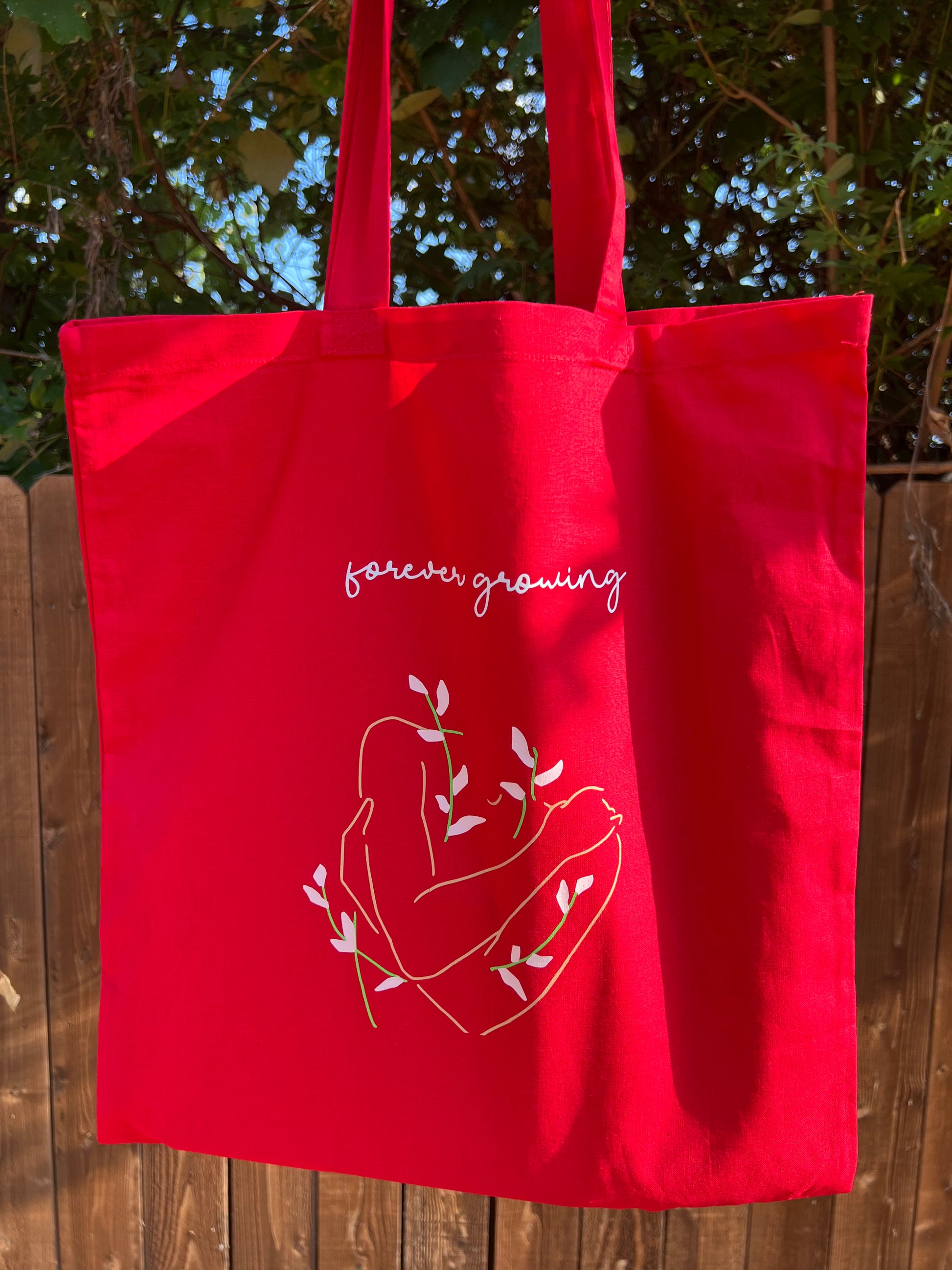 red tote bag with white text and designs in front of brown fence 