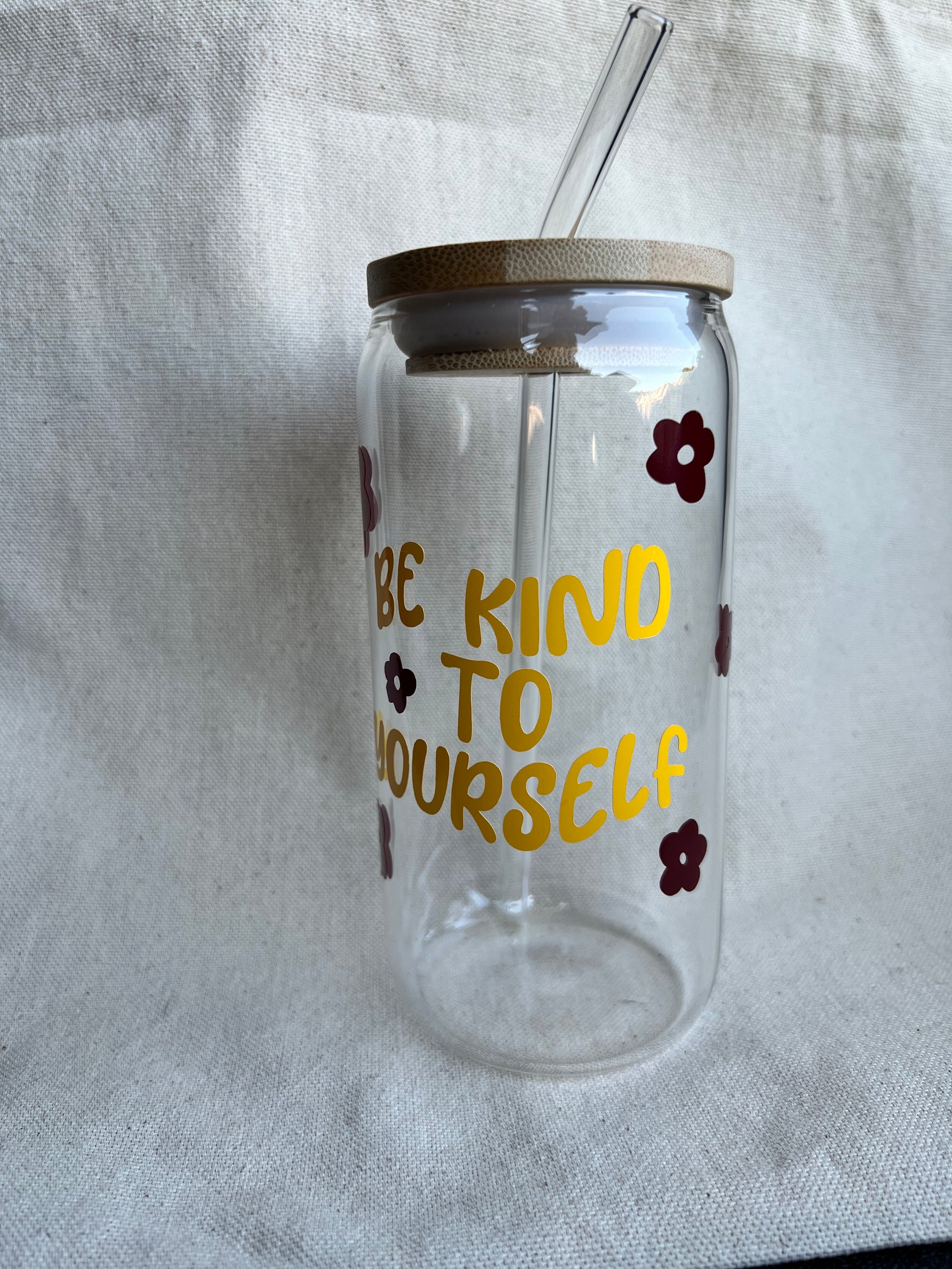 16 oz glass can with bamboo lid and glass straw with yellow and maroon designs in front of natural background
