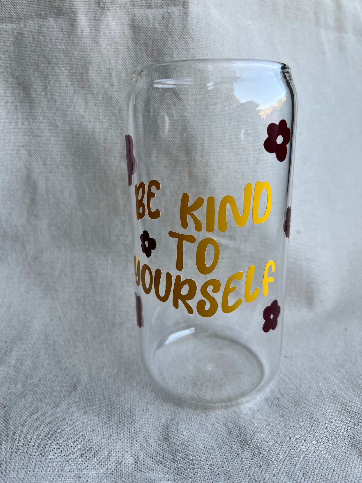 16 oz glass can with yellow text and maroon flowers on natural background